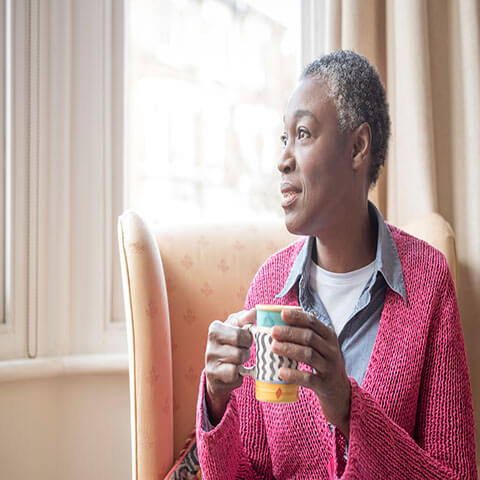A black woman is sitting in a chair and holding a mug